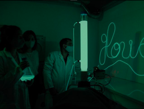 3 researchers in lab with bioluminescent flask and tube